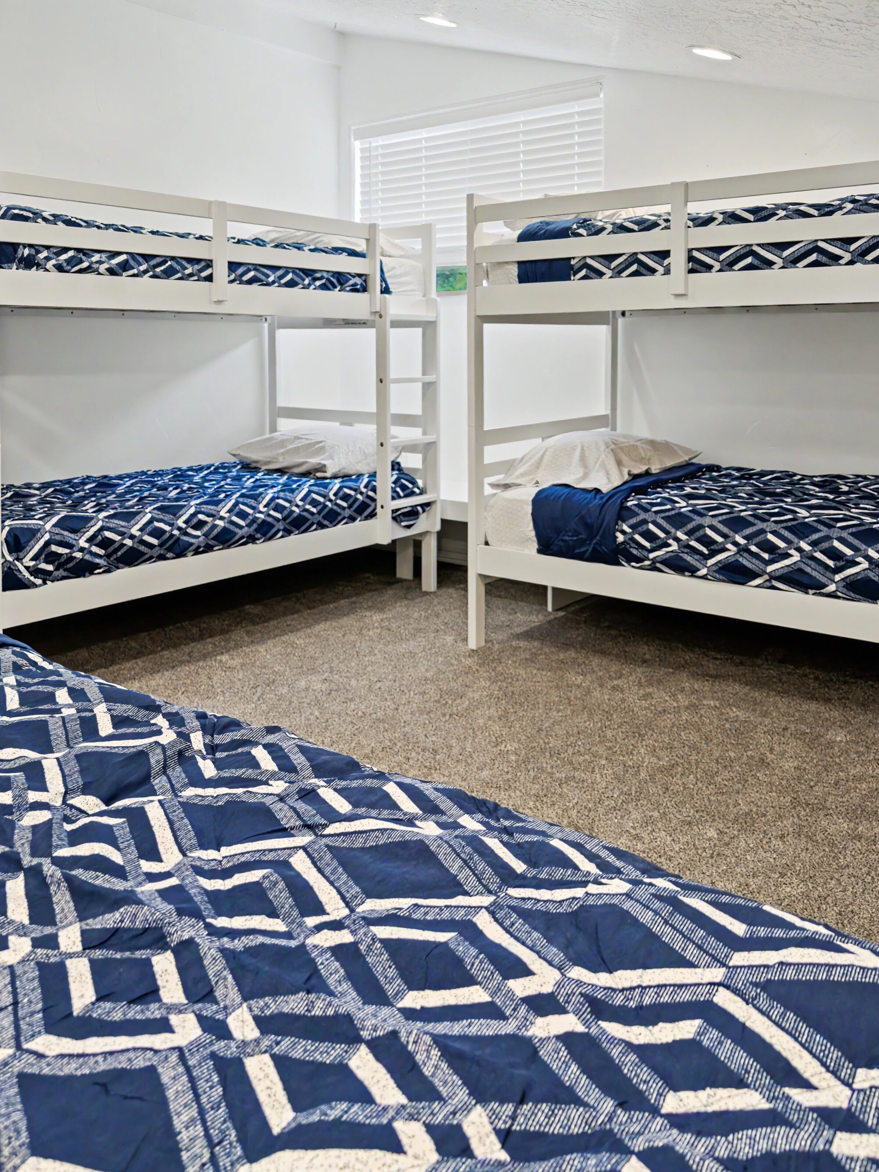A room with bunk beds, a carpeted floor, and a window with blinds.