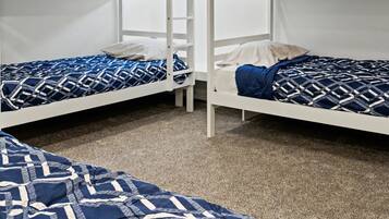 A room with bunk beds, a carpeted floor, and a window with blinds.
