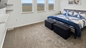 A bedroom with a bed, a ceiling fan, and three windows with a view of the landscape.