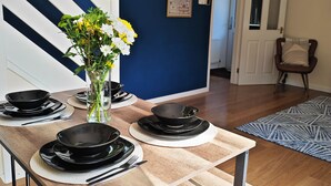 Un coin repas avec une table dressée pour quatre personnes, un vase rempli de fleurs et un mur bleu orné d’un tableau encadré.