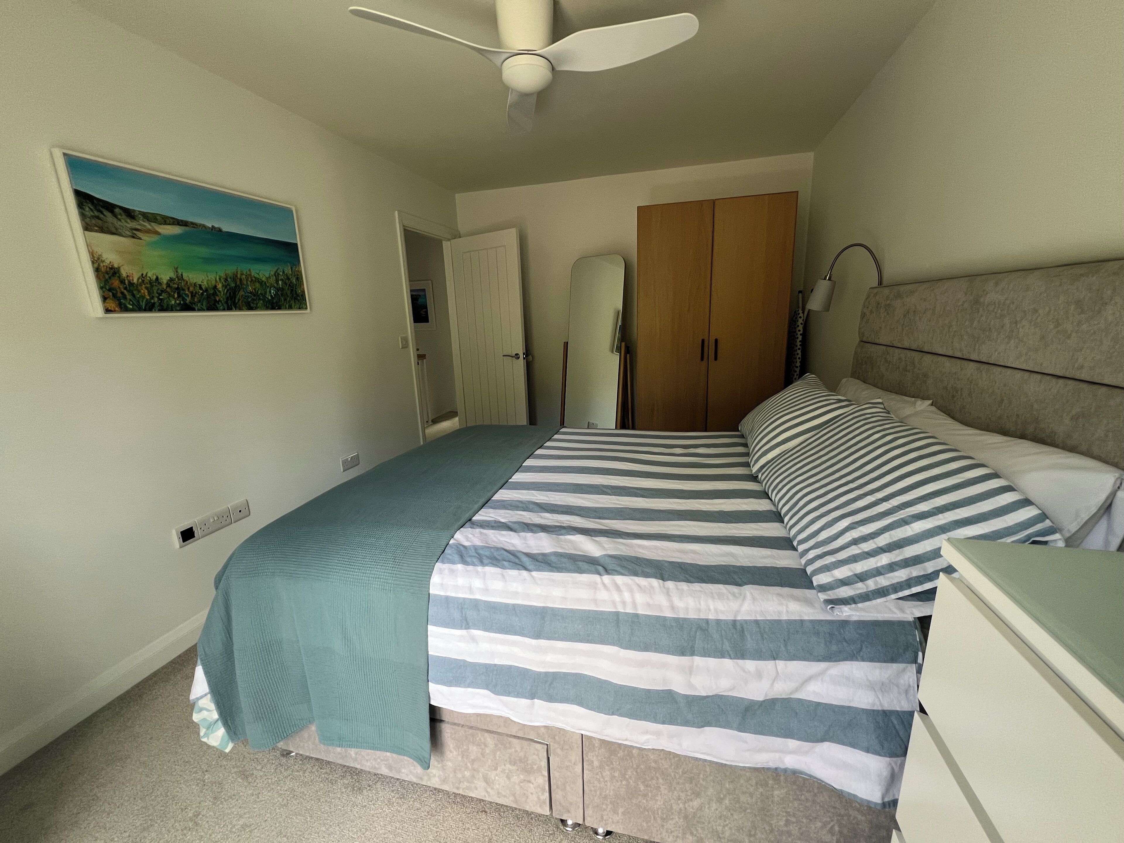 A bedroom with a bed, a ceiling fan, a wardrobe, and a painting on the wall.