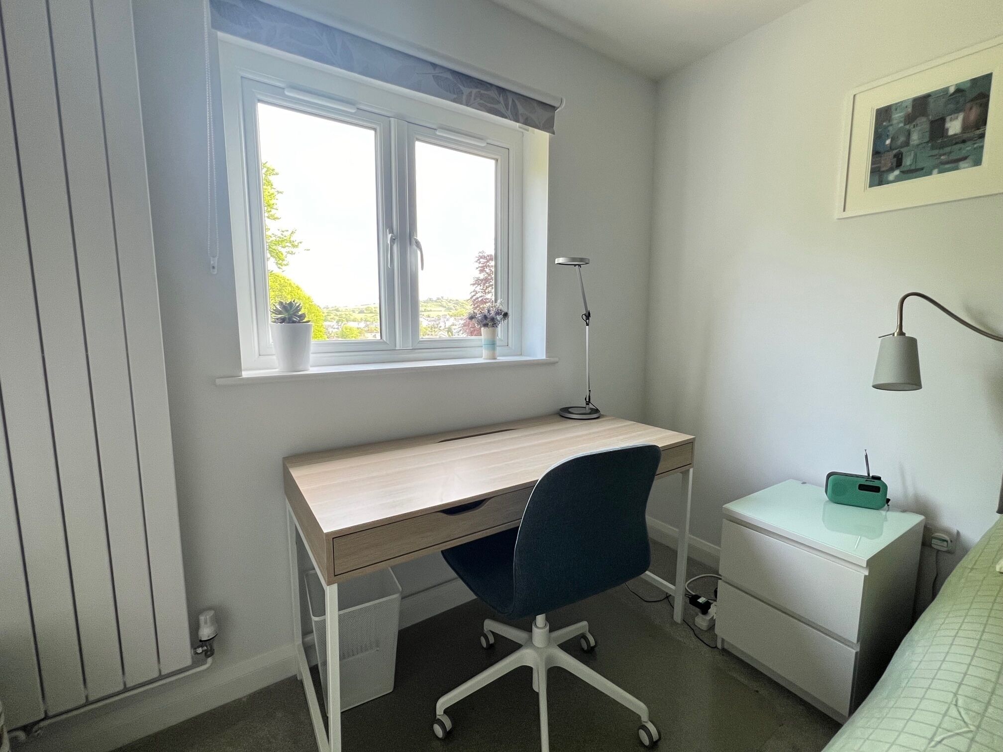 Ein Schlafzimmer mit Bett, Schreibtisch mit Stuhl, Fenster und Nachttisch.