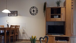 A dining area with a round table, chairs, a wall clock, a television, and a cabinet.