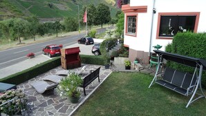 A residential property with a stone patio, outdoor seating, a garden, and a view of a road with parked cars.
