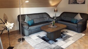 A living room with two black leather sofas, a coffee table, a floor lamp, and a painting on the wall.