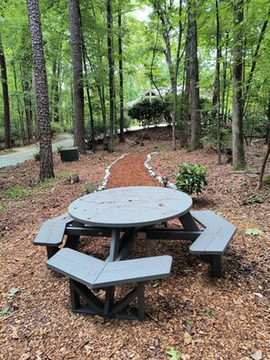 A picnic table with benches in a forested area. - Garden Ensuite at the Chapel Hill Retreat Center (Chapel Hill)