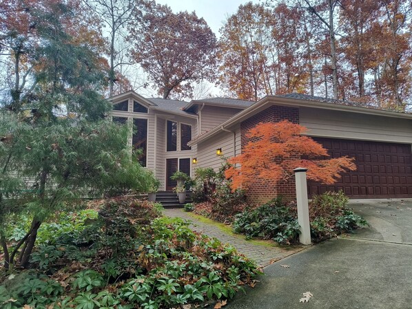 A two-story house with a garage, surrounded by a garden with various plants and trees. - Garden Ensuite at the Chapel Hill Retreat Center (Chapel Hill)