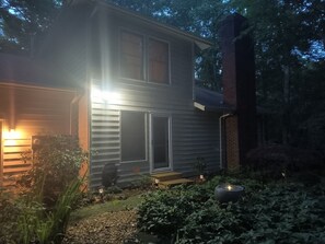 A two-story house with a large window and a door, surrounded by greenery and a small garden area. - Garden Ensuite at the Chapel Hill Retreat Center (Chapel Hill)