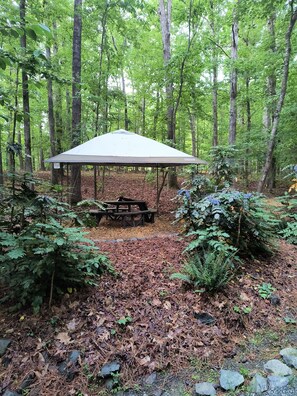 A forested area with a covered picnic table and a shelter. - Garden Ensuite at the Chapel Hill Retreat Center (Chapel Hill)