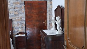 Una habitación con un armario de madera, un aparador, una mesita de noche con una lámpara y una pared de piedra.
