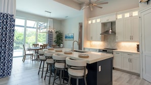 A modern kitchen with white cabinets, a large island with bar stools, and a ceiling fan. - WALK or BIKE to Beach, HEATED & PRIVATE pool & jacuzzi. NEWLY built & stunning. (Marco Island)