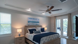A bedroom with a bed, nightstands, a ceiling fan, a painting, and a view through a glass door. - WALK or BIKE to Beach, HEATED & PRIVATE pool & jacuzzi. NEWLY built & stunning. (Marco Island)