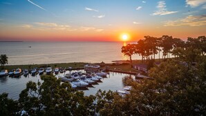 A marina with boats docked, a sunset over the water, and trees in the foreground.