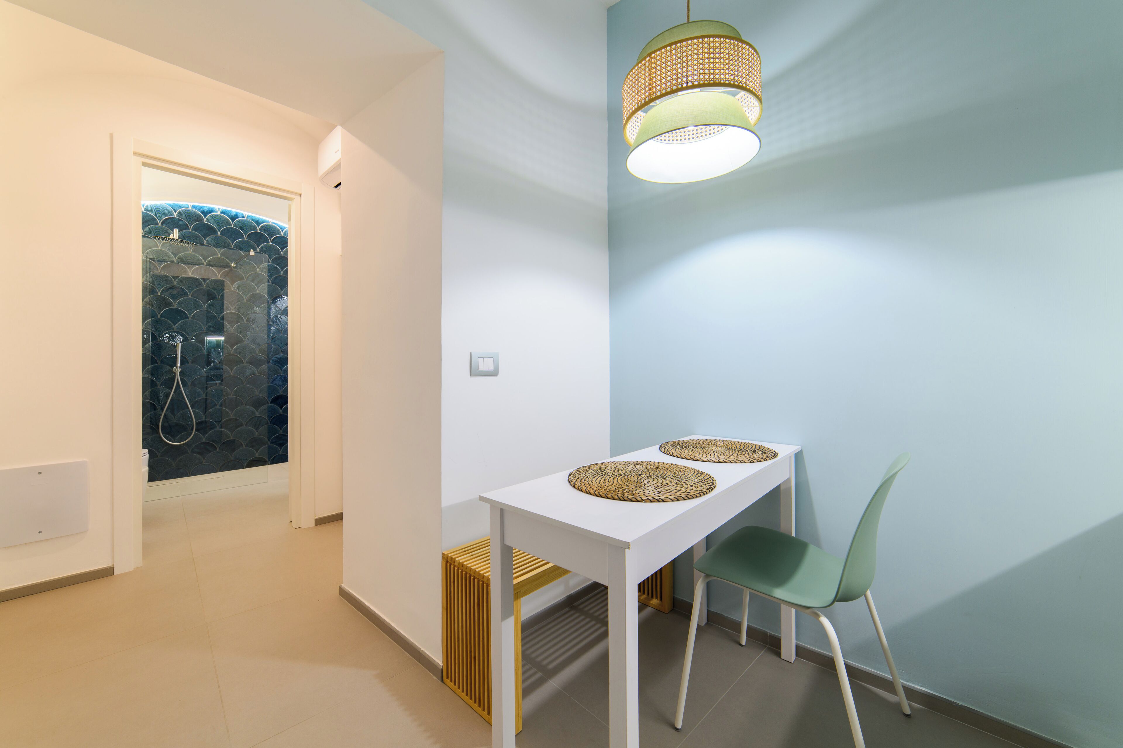 Un baño moderno con ducha, una mesa blanca con dos individuales tejidos, y una silla verde.