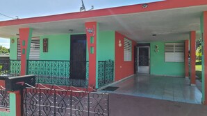 Un edificio con fachada roja y verde, un acceso cubierto y una verja metálica.