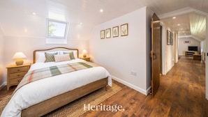 A bedroom with a large bed, bedside lamps, a window, and a hallway leading to a living area. - The Byre, Countryside Home (Tough)
