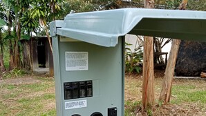 An electrical panel with switches and a meter, surrounded by grass and trees.