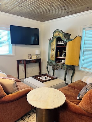 A living room with a brown sofa, a round coffee table, a television mounted on the wall, and a decorative cabinet with glassware. - Stay in the Heart of historic Georgetown! (Georgetown)