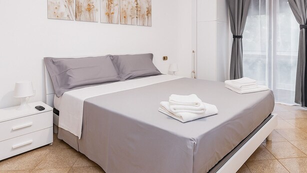 Une chambre moderne avec un grand lit, des tables de chevet blanches et une fenêtre avec des rideaux.