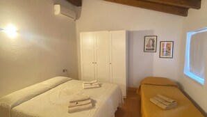Una habitación con dos camas, un armario y un pequeño banco.