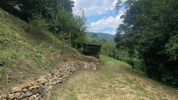 Eine steinerne Stützmauer mit einer kleinen Schutzhütte, umgeben von dichtem Grün und blauem Himmel.