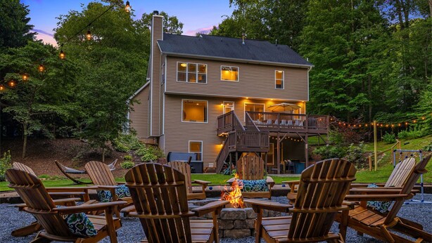 A two-story house with a deck, outdoor seating area with Adirondack chairs, and a fire pit. - Spacious & Luxe~Hot Tub~Bocce~Fenced Backyard~Mins to Downtown! (Asheville)