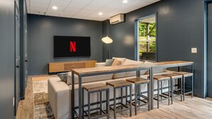 A modern living room with a large flat-screen TV mounted on the wall, a wooden coffee table, and a sofa with matching cushions. - Spacious & Luxe~Hot Tub~Bocce~Fenced Backyard~Mins to Downtown! (Asheville)