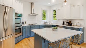 A modern kitchen with white cabinets, a stainless steel refrigerator, a central island, and blue cabinetry. - Spacious & Luxe~Hot Tub~Bocce~Fenced Backyard~Mins to Downtown! (Asheville)