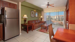 Un espace de vie compact comprenant un coin cuisine, un canapé, une table à manger et un balcon avec vue sur les immeubles.