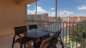 Un balcon avec une table ronde et quatre chaises, donnant sur une étendue d’eau et un complexe hôtelier.