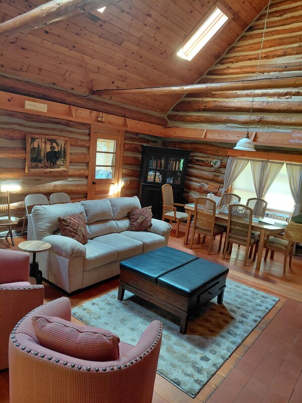 A log cabin interior with a sofa, chairs, a dining table, and a bookshelf.