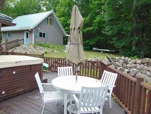 A deck with a hot tub, white chairs, and a table.