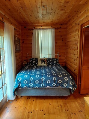 A wooden cabin bedroom with a bed, curtains, and a window.