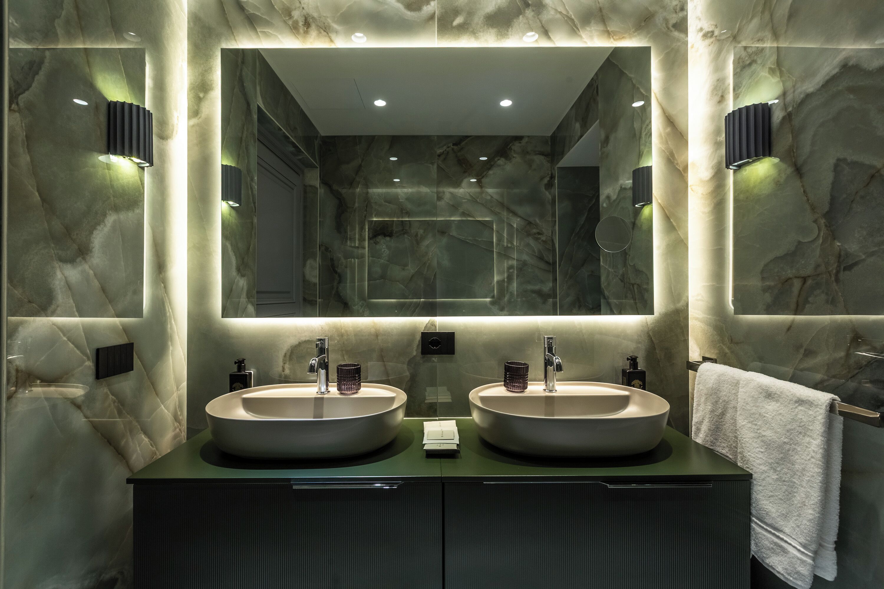 Un baño moderno con dos lavamanos, un espejo grande y paredes de mármol.