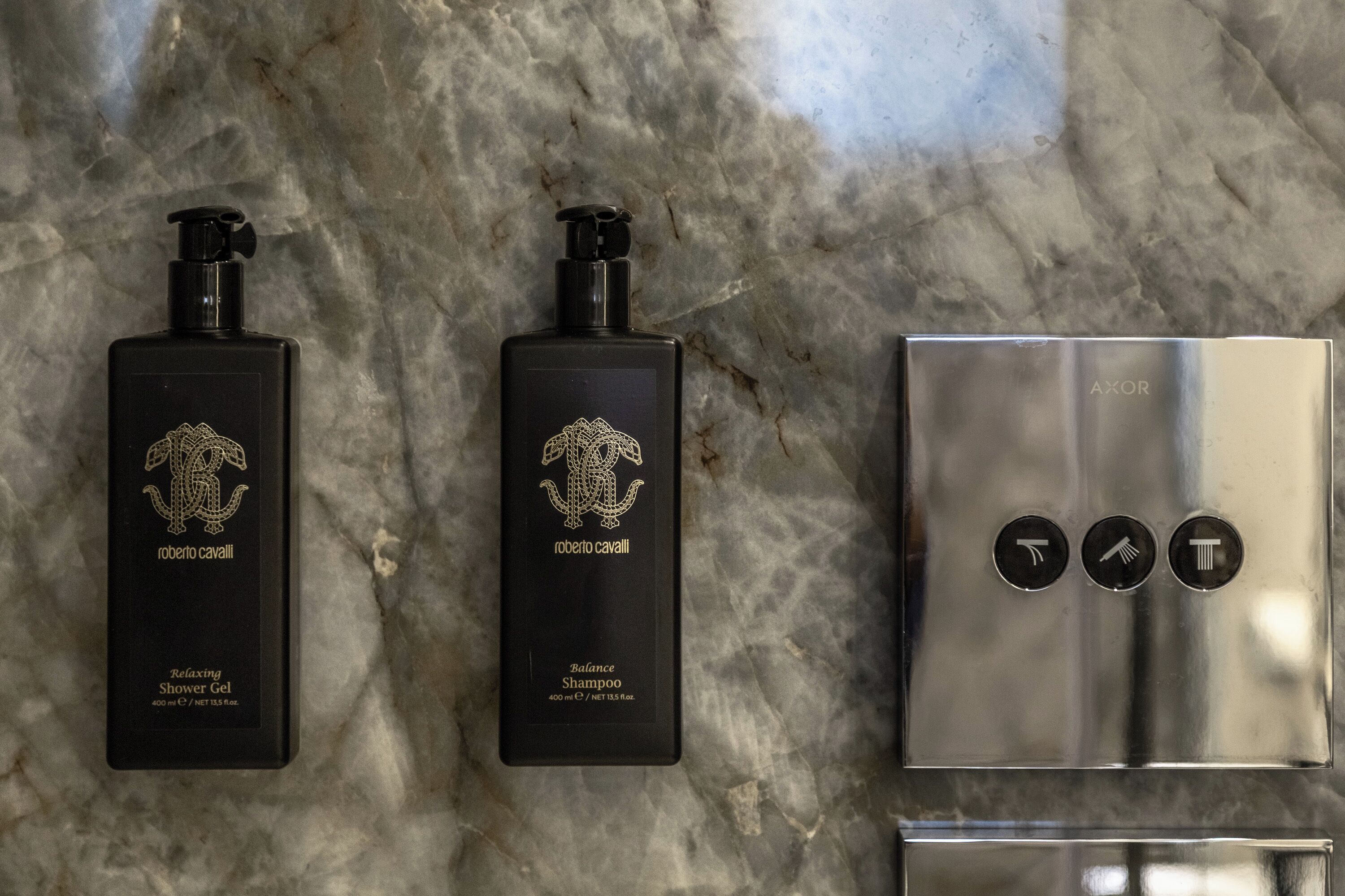 Two black bottles of Roberto Cavalli products on a marble surface, and a metallic object with symbols.