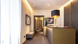 A hotel hallway with a reception desk, a bench, framed artwork, and a large mirror. - Fontart Tritone  (Rome)
