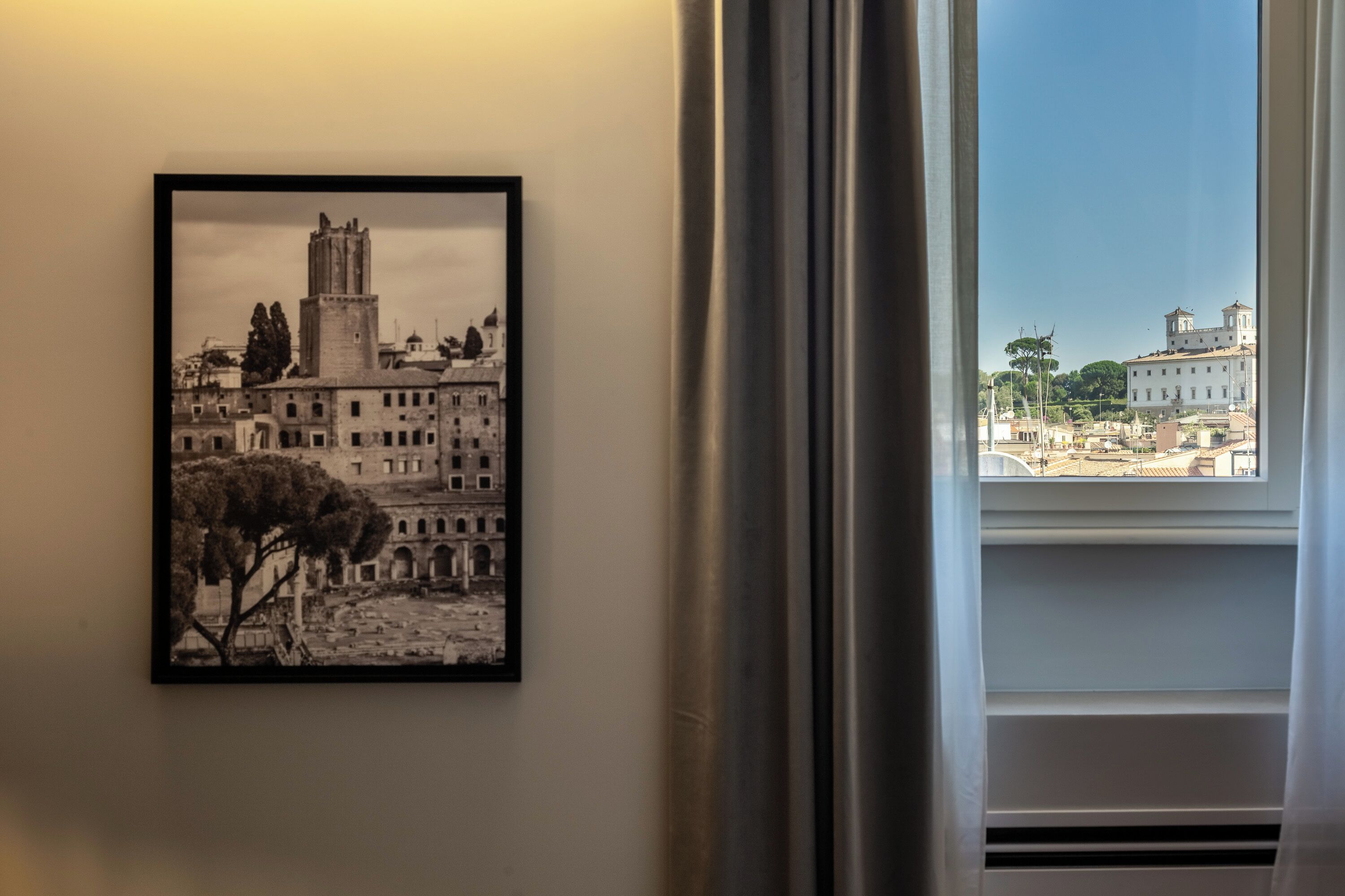 A framed black and white photograph of a historic building with a tower, displayed on a wall next to a window with curtains.