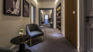 A hallway with a modern chair, a small table with a vase, and framed artwork on the walls. - Fontart Tritone  (Rome)