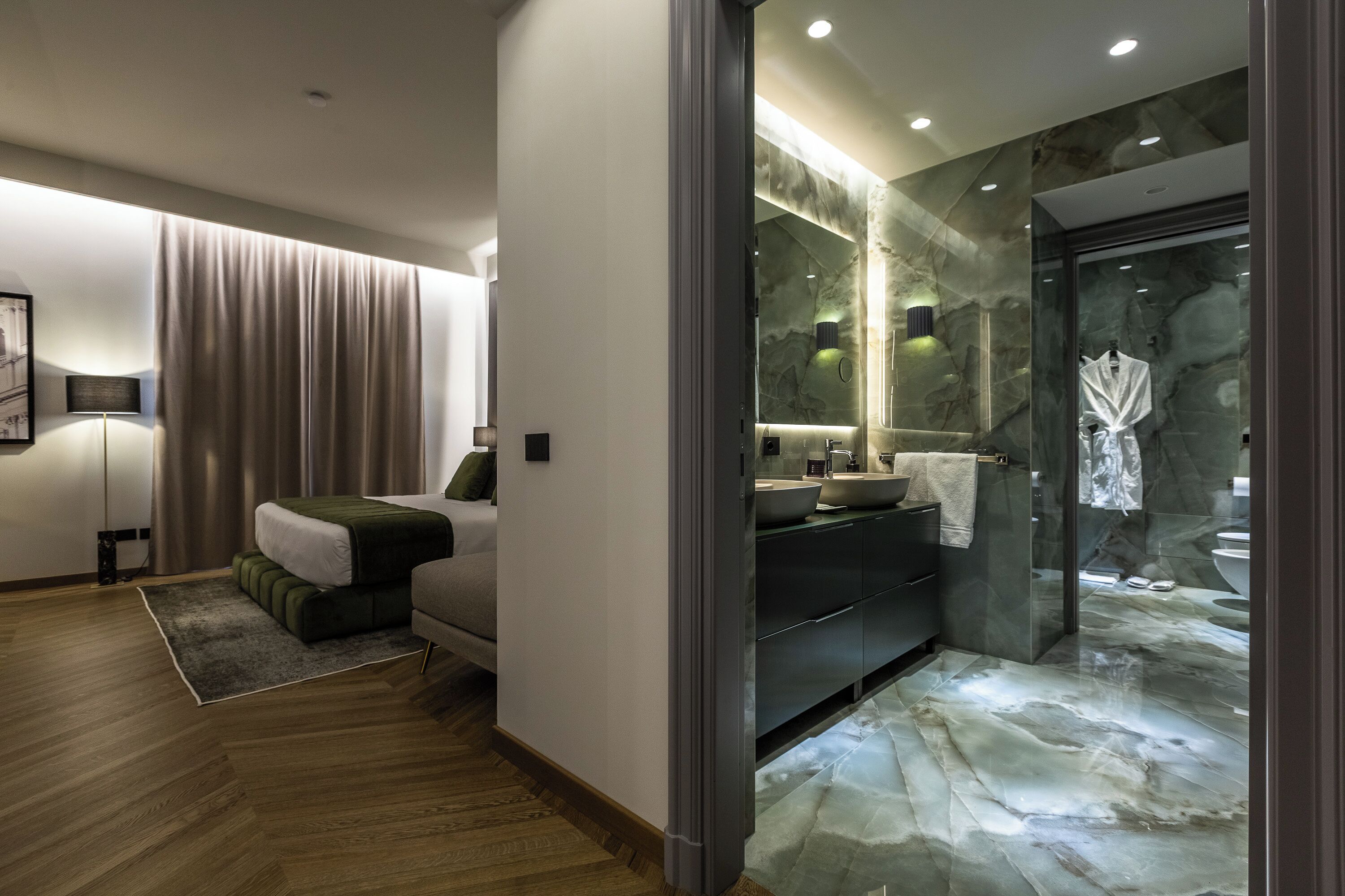 Een moderne hotelkamer met een bed, een zithoek, een badkamer met een douchecabine van glas en een marmeren vloer.
