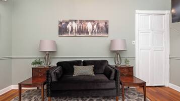 A living room with a dark sofa, two side tables with lamps, a leopard print rug, and a wall-mounted horse painting.