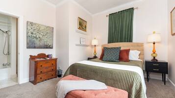 Een slaapkamer met een bed, twee nachtkastjes, een dressoir, een bijzettafeltje, een lamp, een schilderij en een douchegedeelte.