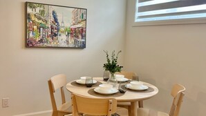 Ein Essbereich mit einem runden Tisch, vier Stühlen, einer Blumenvase und einem Gemälde einer Straßenszene an der Wand.