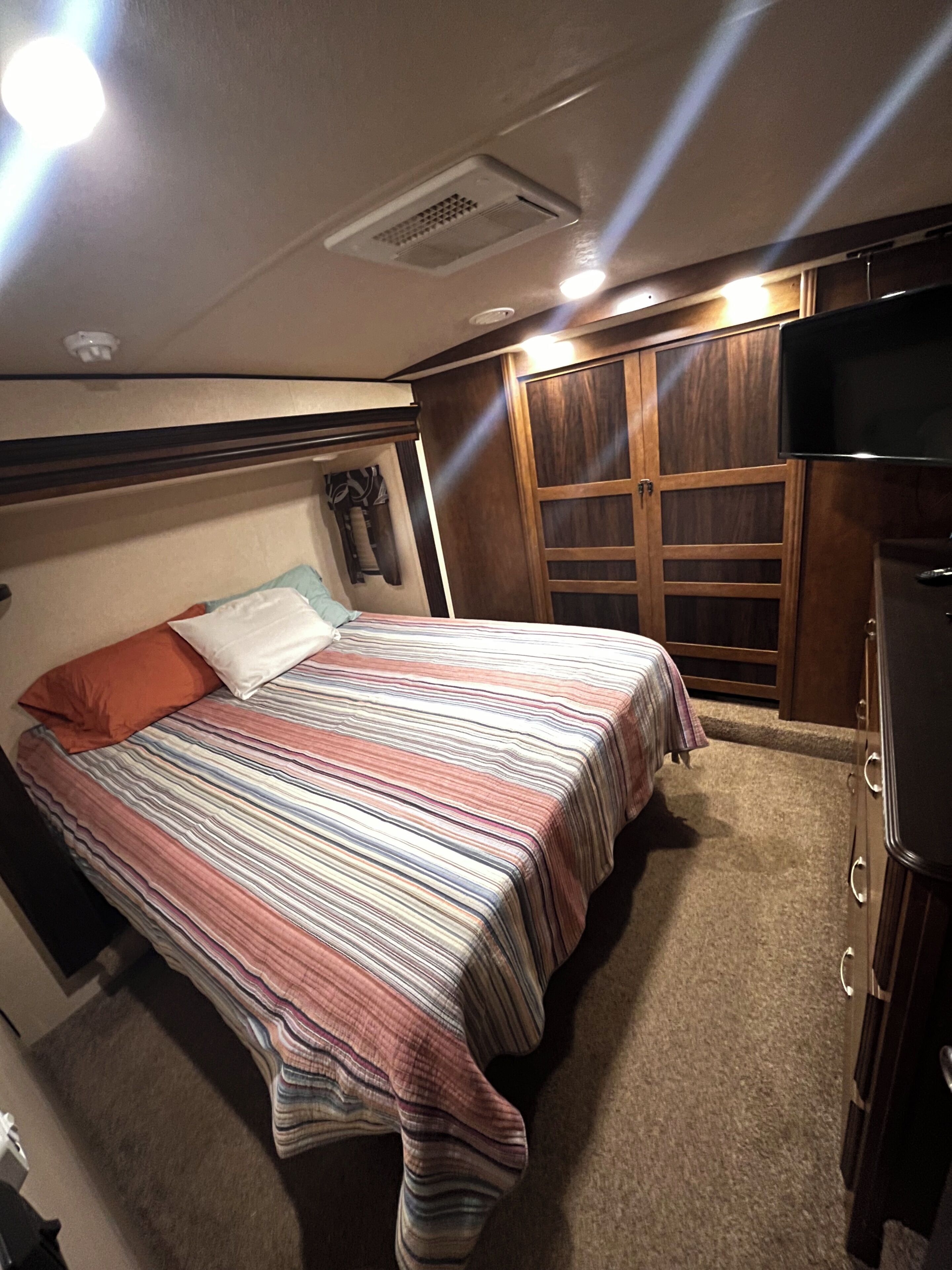 A bedroom with a bed, a wardrobe, a television, and a ceiling vent.