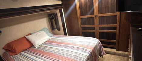 A bedroom with a bed, a wardrobe, a television, and a ceiling vent.