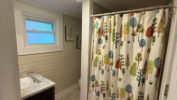 A bathroom with a window, a sink, a shower curtain with tree patterns, and red rugs.
