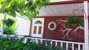 A porch with a red door, white railings, and hanging planters.