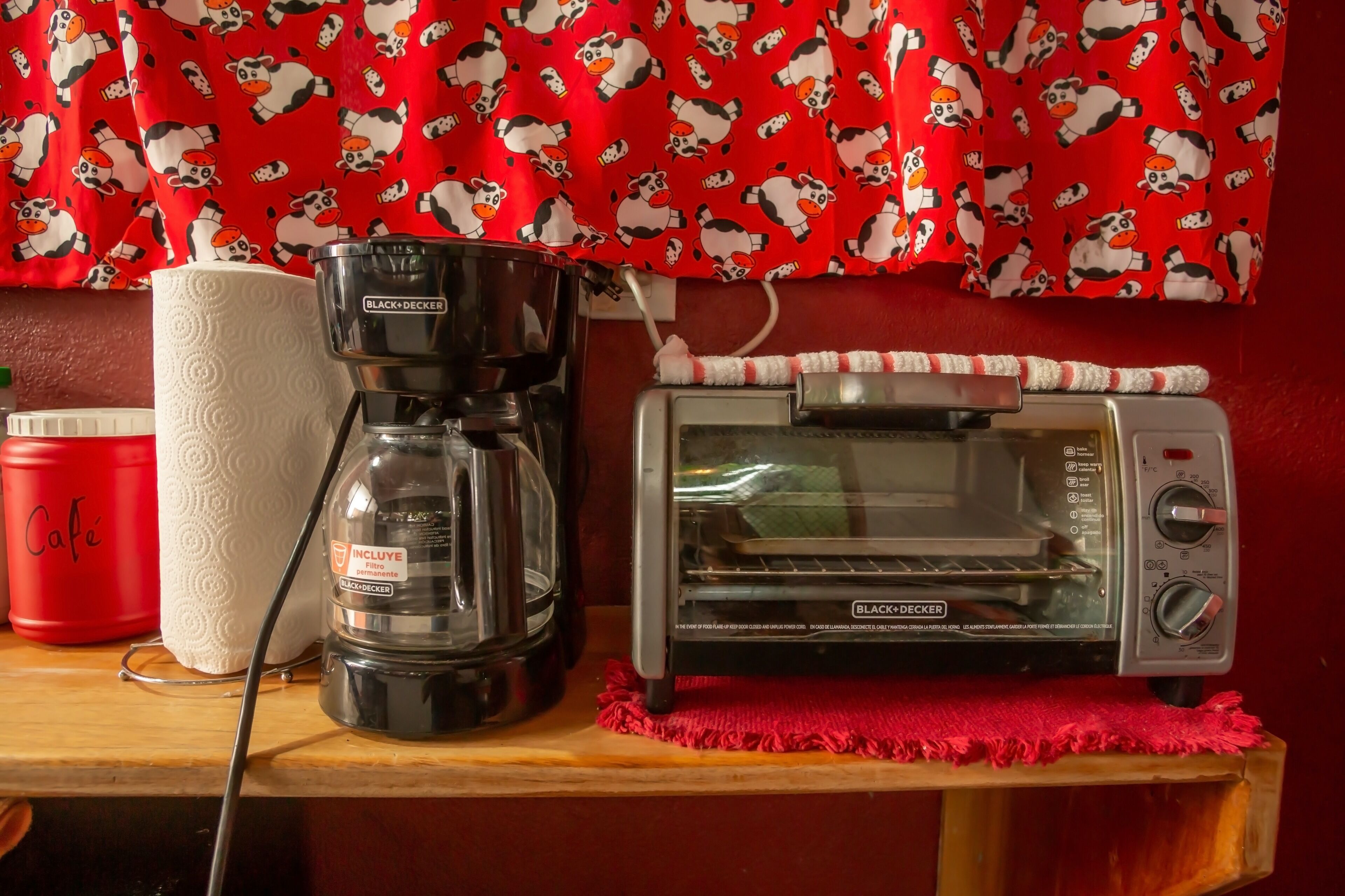 A kitchen counter with a coffee maker, a toaster, a red container labeled "Cafe", and a roll of paper towels.