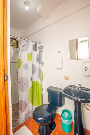 A bathroom with a toilet, sink, and shower curtain. - Hostal Nuevo Arenal (Nuevo Arenal)