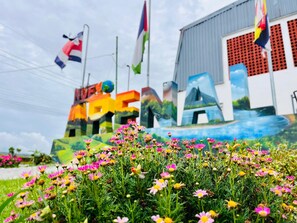 A colorful outdoor area with a large mural featuring letters and a globe, surrounded by vibrant flowers. - Hostal Nuevo Arenal (Nuevo Arenal)