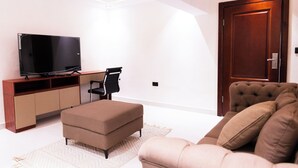 Un salon moderne avec un téléviseur à écran plat posé sur un meuble en bois, un canapé marron, un pouf assorti et une grande porte en bois.